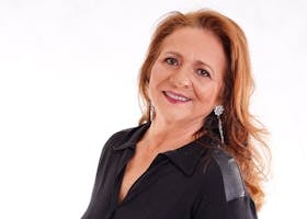 Portrait of a smiling senior woman with long hair and earrings in a black outfit.